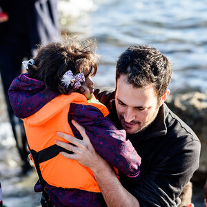 A man is carrying a child wearing a lifejacket to safety—a photo of Yotam Polizer.