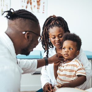 A young boy seated on his mother's lap is being examined by his doctor. A young boy seated on his mother's lap is being examined by his doctor.