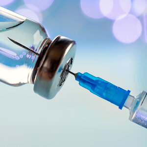 A needle inserted into a vial containing a vaccine.