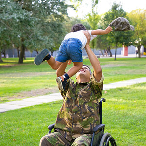 A veteran holding a young girl above him.