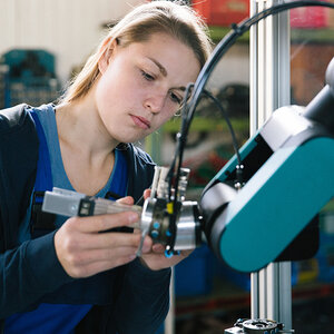 A female student repairs a robotic arm on the factory floor. A female student repairs a robotic arm on the factory floor.