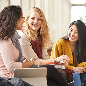 Three smiling female college students sit together talking. Three smiling female college students sit together talking.
