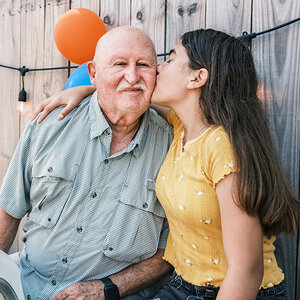 A granddaughter kisses her grandfather on the cheek at a party.