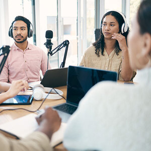 A group of journalists talking into podcast microphones. A group of journalists talking into podcast microphones.