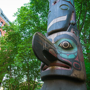 An Indigenous totem pole in a public square surrounded by trees and buildings.