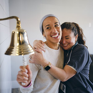 A woman ringing a bell in the hospital, embraced by a nurse. A woman ringing a bell in the hospital, embraced by a nurse.