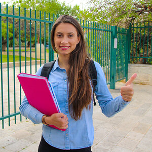 A high school student holding a notebook and giving a thumbs up sign with her hand.
