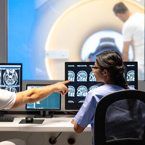 Brain scientists view a computer screen with an MRI machine in the background.