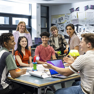 High school students and their teacher sitting in a group in a classroom.
