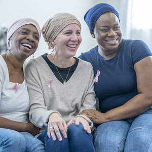 Three women with breast cancer are wearing pink ribbons on their shirts and smiling