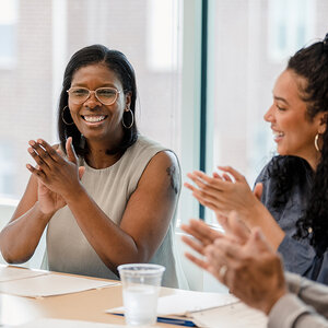A woman applauding at a board room table. A woman applauding at a board room table.