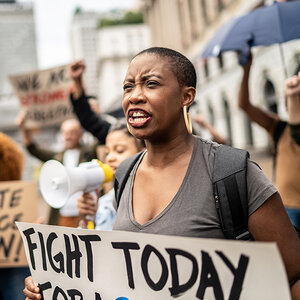 An African American woman at a protest rally holds a placard reading Fight Today. An African American woman at a protest rally holds a placard reading Fight Today.