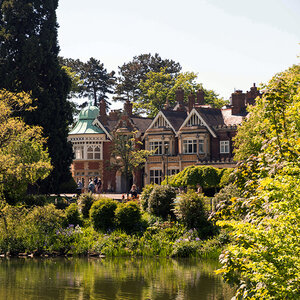 A Victorian mansion surrounded by trees and a pond in a park-like setting – Bletchley Park.