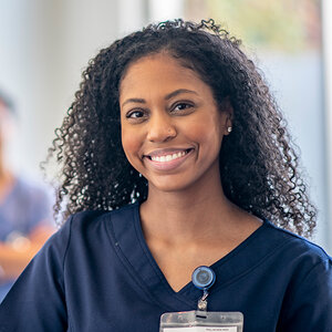 A female student in hospital scrubs smiles at the camera.