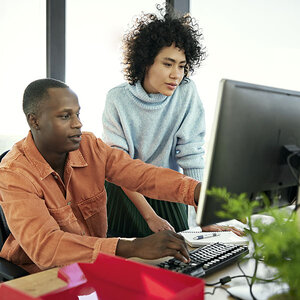 Two people working on a computer in an office.