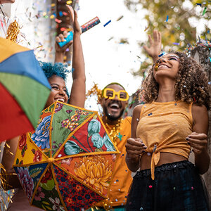 Three people of color wearing festive clothing and carrying colorful umbrellas.