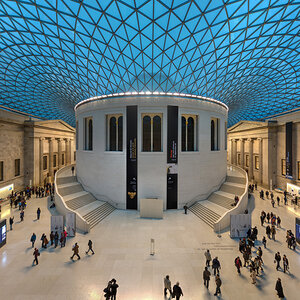 The entry court of a museum with a modern blue-glass lattice roof suspended over the facades of neoclassical buildings – the British Museum.