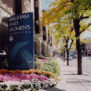The entrance to a hospital on a street lined with trees and flowers with a sign that reads Brigham and Women’s Hospital.