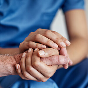 A medical professional in blue scrubs holding a patient's hand. A medical professional in blue scrubs holding a patient's hand.