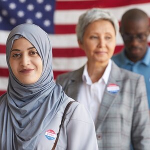 Diverse voters standing in line in front of an American flag. Diverse voters standing in line in front of an American flag.