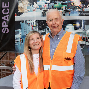 An older man and his adult daughter wearing orange safety vests in front of a museum display - a photo of Kent Kresa and Kiren Kresa-Reahl.