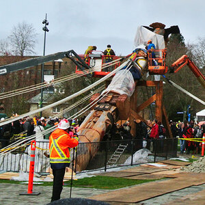 Workers raise a totem pole as a crowd of people watch. Workers raise a totem pole as a crowd of people watch.