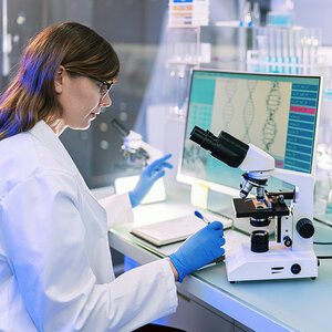 A female scientist in a lab studies DNA using a microscope. A female scientist in a lab studies DNA using a microscope.