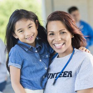 Young girl with woman of color wearing T-shirt that says 'VOLUNTEER.'