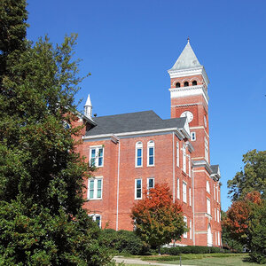 An old brick building with a clocktower on a college campus surrounded by trees.