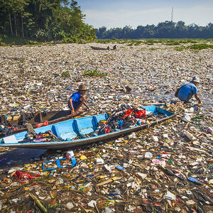 Two people in a boat wading through plastic waste in a waterway. Two people in a boat wading through plastic waste in a waterway.