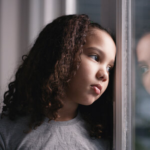 A sad young girl looking out a window.