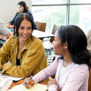 Two female college students studying together at a table. Two female college students studying together at a table.
