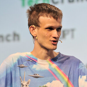 A man wearing a colorful t-shirt speaks on stage - a photo of Vitalik Buterin. A man wearing a colorful t-shirt speaks on stage - a photo of Vitalik Buterin.
