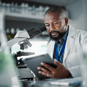 An African scientist in his labe reviews data on a tablet.