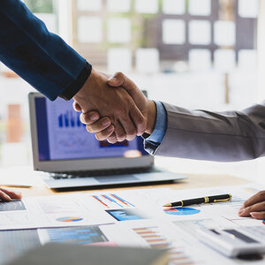 A handshake over a table full of charts and graphs. A handshake over a table full of charts and graphs.