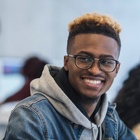 An African American college student with glasses smiles and looks to his right. An African American college student with glasses smiles and looks to his right.