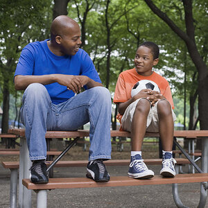 A child of color sits on a picnic table with his mentor