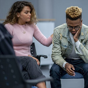 A young man being comforted by a woman, both sitting.