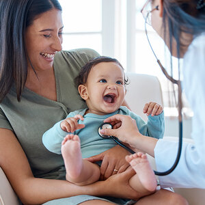 A smiling mother holds her baby as a doctor performs a wellness exam.