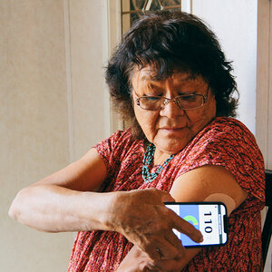 An older woman wearing glasses checks her glucose level with her mobile phone. An older woman wearing glasses checks her glucose level with her mobile phone.