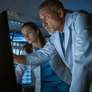 Two physician scientists, one male and one female, look at a computer monitor.