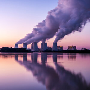 A powerplant releasing clouds of gas in the sunset.