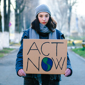 A young woman holding a climate-change protest sign that reads: Act Now. A young woman holding a climate-change protest sign that reads: Act Now.