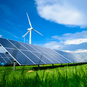 Solar panels and a wind turbine behind it in a field of green grass.