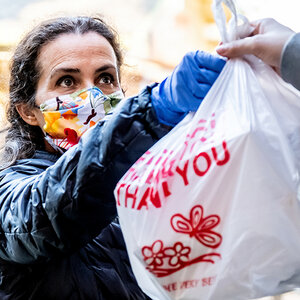 A woman wearing a mask receives a bag of food with the words "Thank you" on the bag.