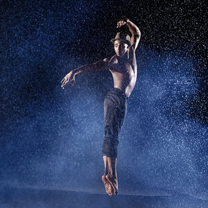 A male dancer performing on a darkened stage.