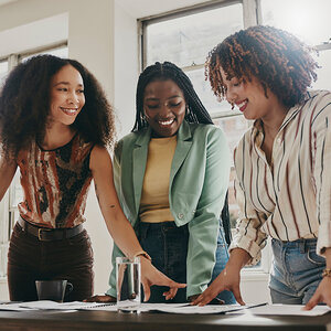 Three African-American women point to documents on a table. Three African-American women point to documents on a table.