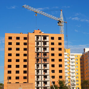 A high-rise apartment building under construction beneath a deep blue sky.