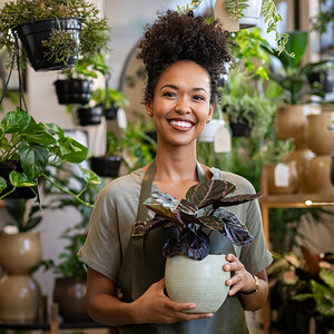 The female owner of a plant store is wearing an apron and holding a potted plant.