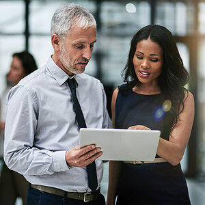 A white man with gray hair and a woman of color consult together. A white man with gray hair and a woman of color consult together.
